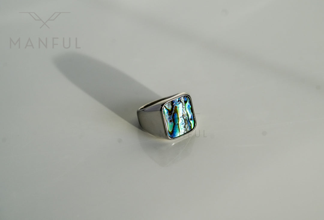 Abalone Shell Signet Ring, lying on a white surface with a long shadow stretching behind it