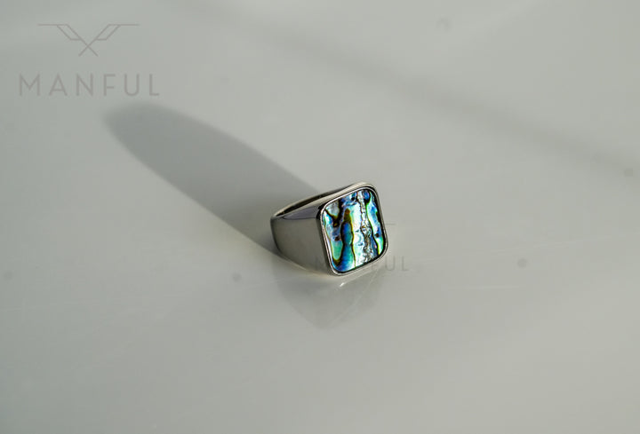 Abalone Shell Signet Ring, lying on a white surface with a long shadow stretching behind it