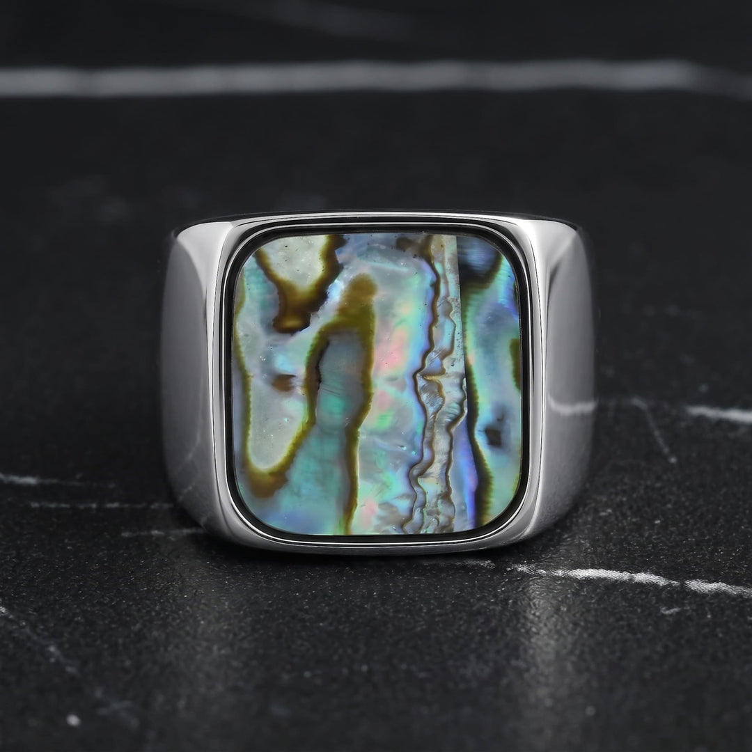 Abalone Shell Signet Ring standing upright on black marble with thin white veins