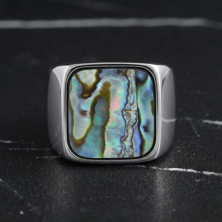 Abalone Shell Signet Ring standing upright on black marble with thin white veins