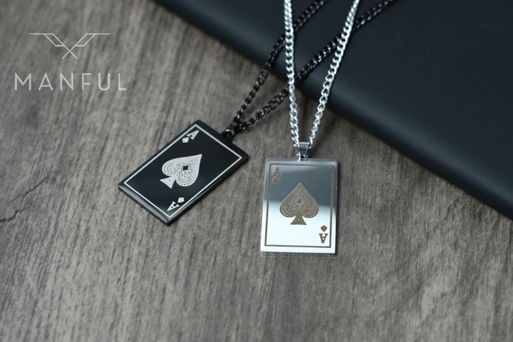 Ace Of Spades Pendant Black, paired with a silver ace pendant on wood beside a phone case