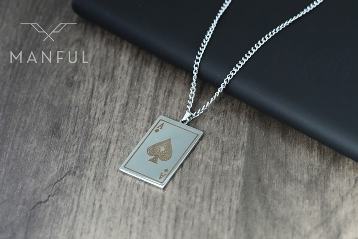 Ace Of Spades Pendant Silver, resting on a wooden surface with a dark case propped behind it