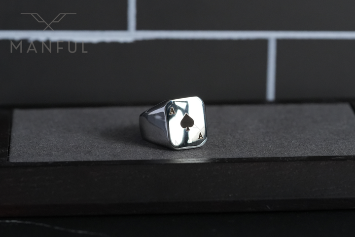 Ace Of Spades Signet Ring, standing on a dark stone block against a brick-patterned wall