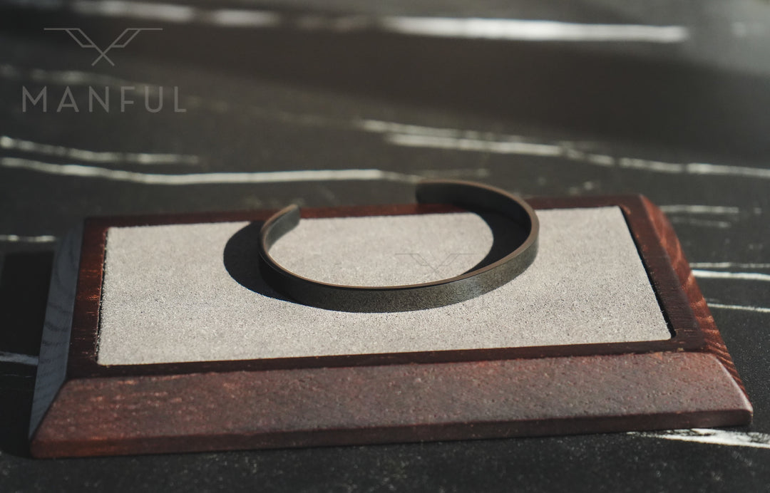 Adjustable Bangle Black, resting on a sand-textured tray with a dark marble backdrop