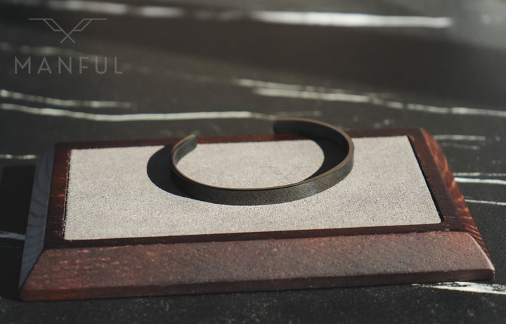Adjustable Bangle Black, resting on a sand-textured tray with a dark marble backdrop
