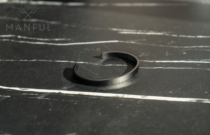 Adjustable Bangle Black, lying open-end down on a dark marble surface