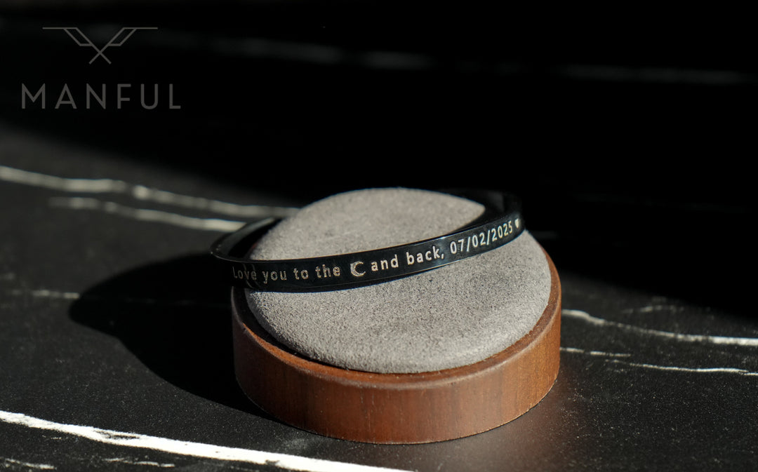 Adjustable Bangle Black, resting on a round cushion with the engraving facing forward