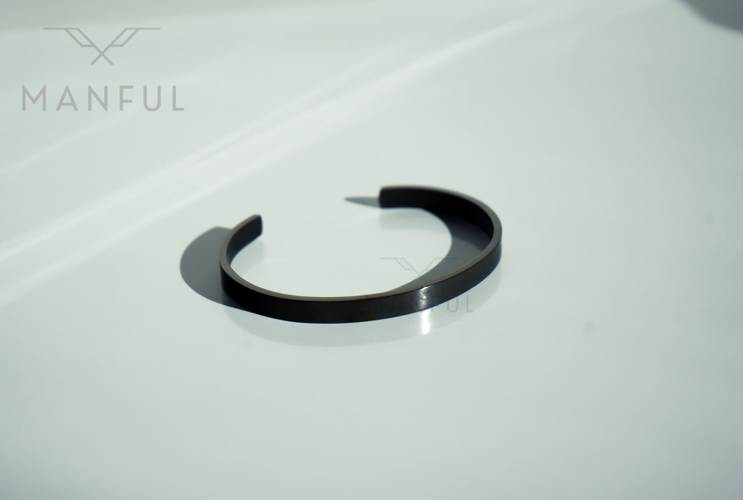 Adjustable Bangle Black, resting on a plain white marble surface
