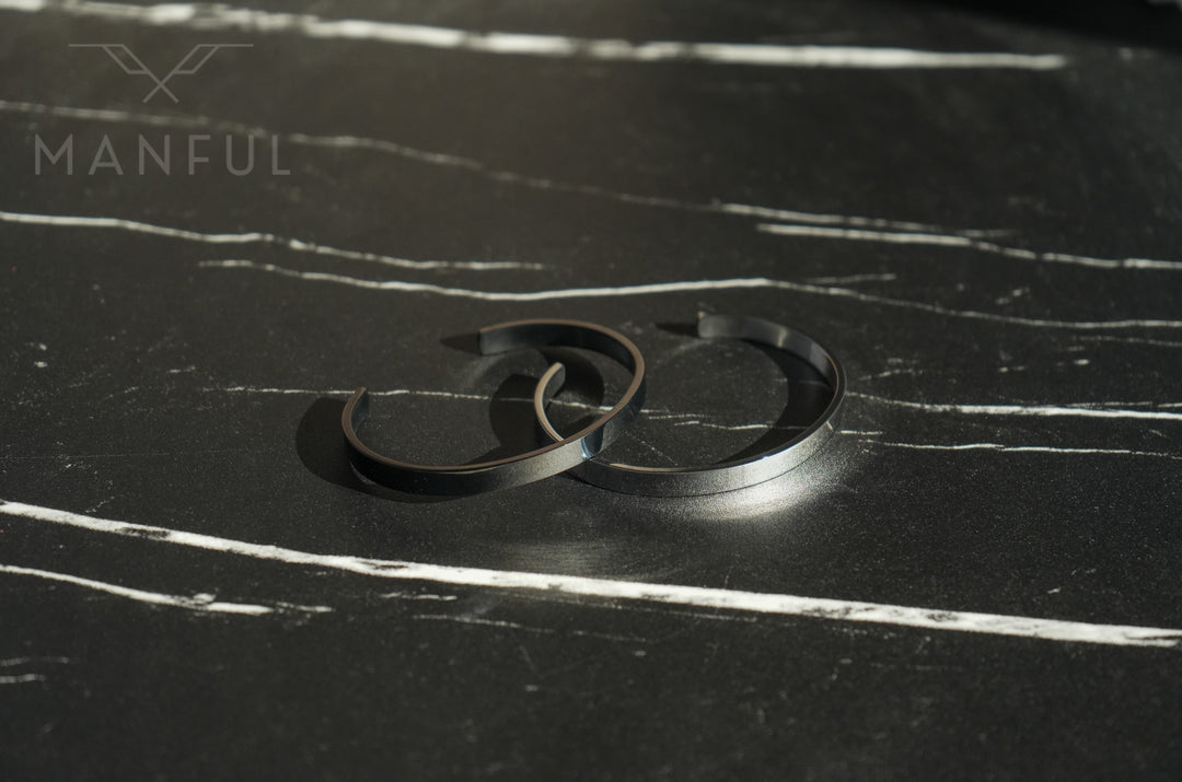 Adjustable Bangle Black, two bangles overlapping on a dark marble surface
