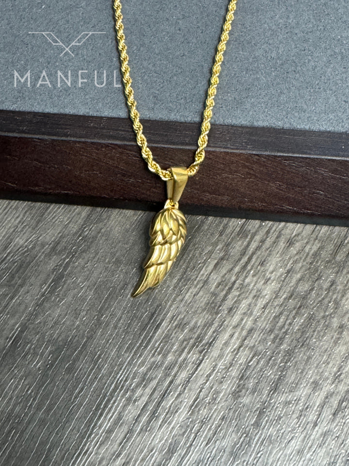 Angel Wing Pendant Necklace Gold, close-up against a stone and wood ledge showing the wing's feather detail