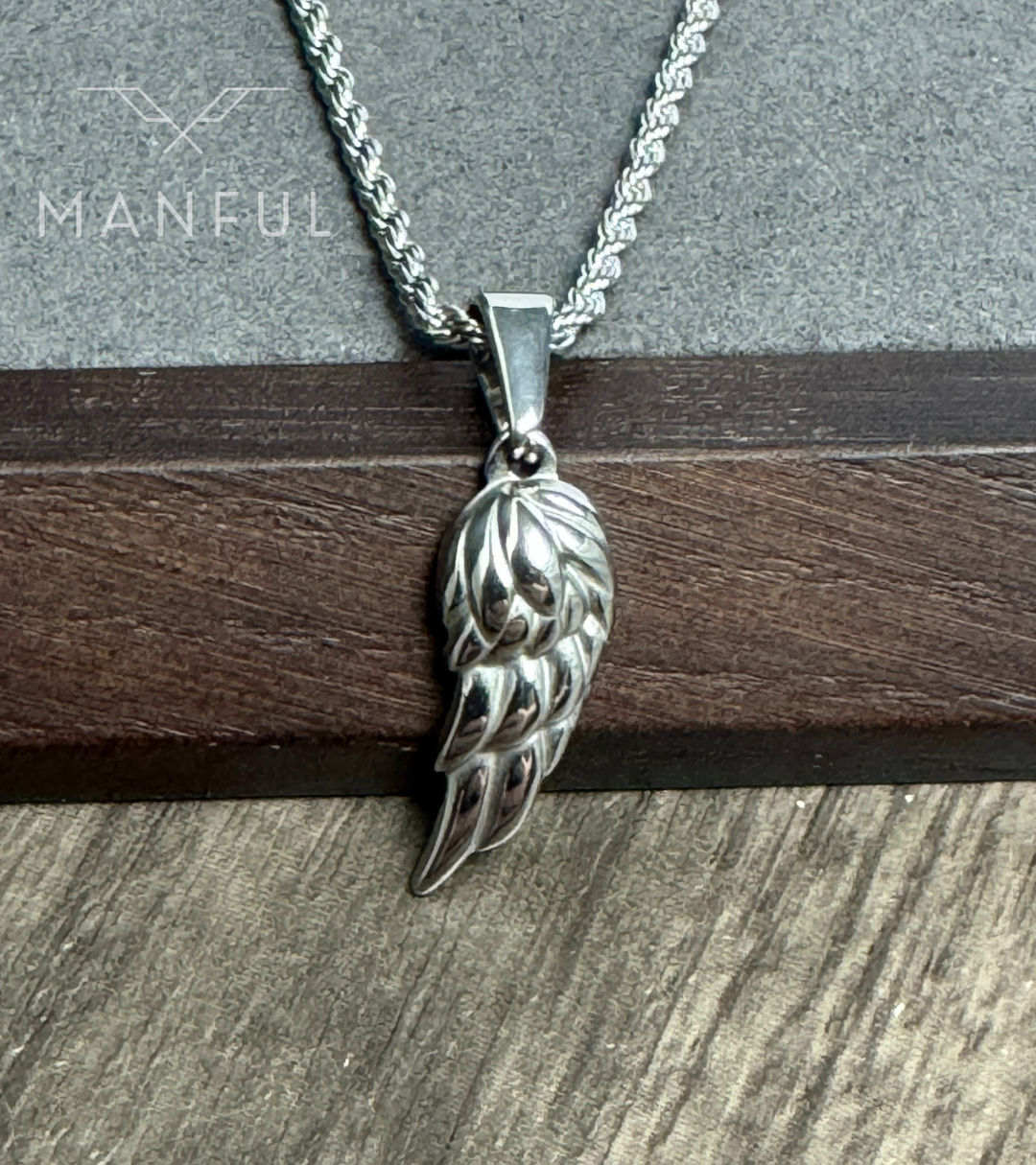 Angel Wing Pendant Necklace Silver, close-up hanging against a wood and stone backdrop