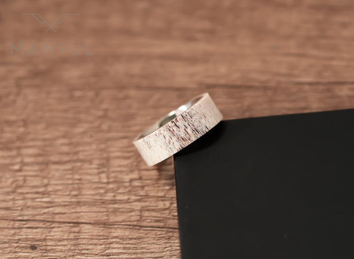 Antler & Titanium Band, leaning against a dark block on a woodgrain surface