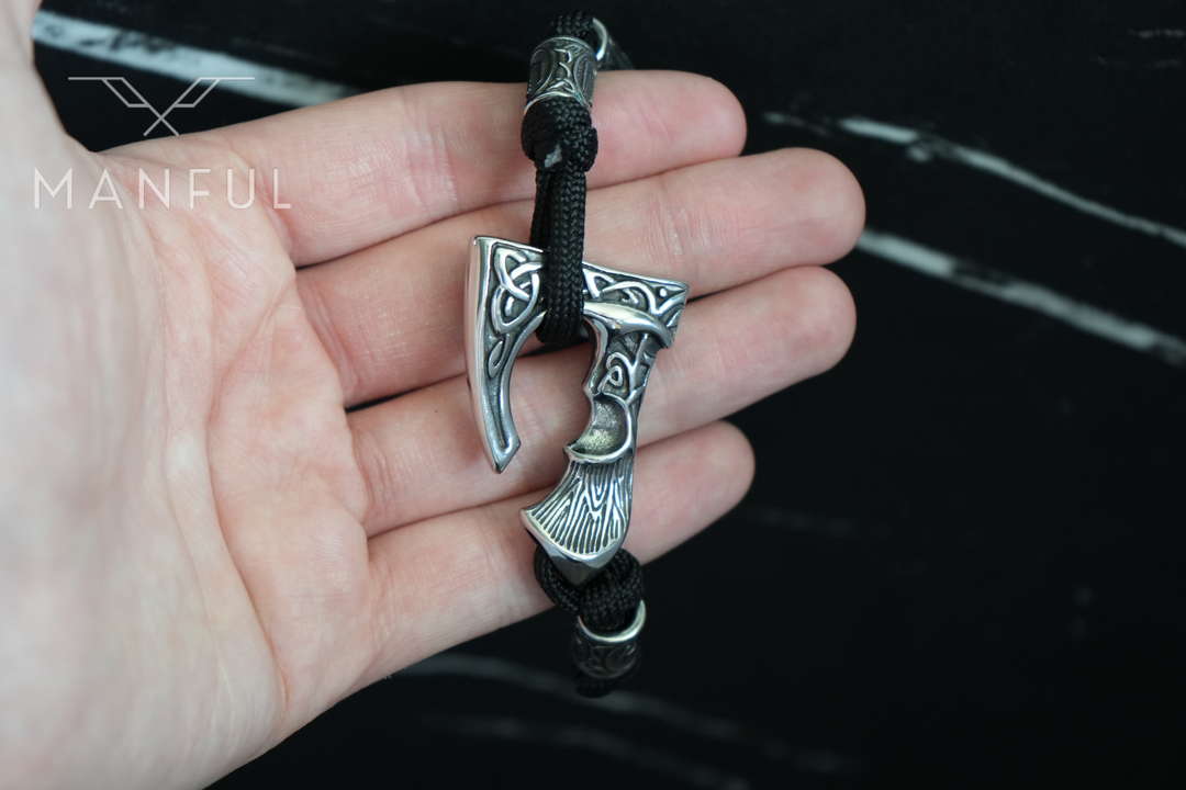 Axe Bracelet, held in a man's hand for a close-up of the axe charm against dark marble