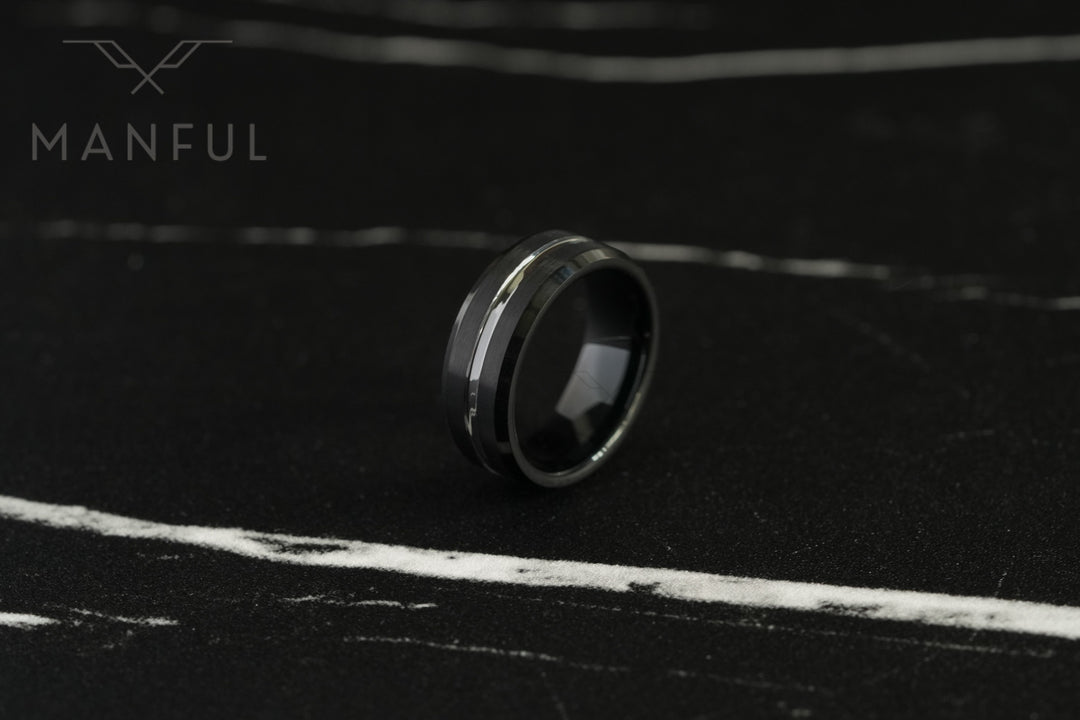 Black and Silver Tungsten Ring, resting at an angle on a dark marble surface