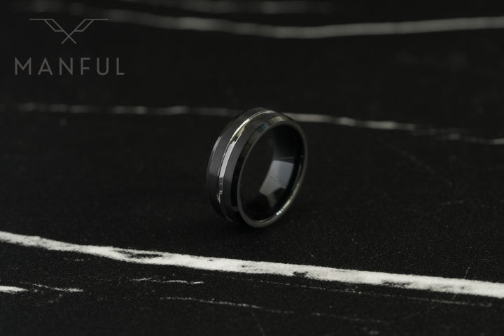 Black and Silver Tungsten Ring, resting at an angle on a dark marble surface