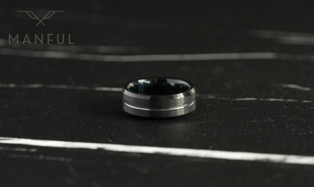 Black and Silver Tungsten Ring, lying flat on a dark marble surface in close-up