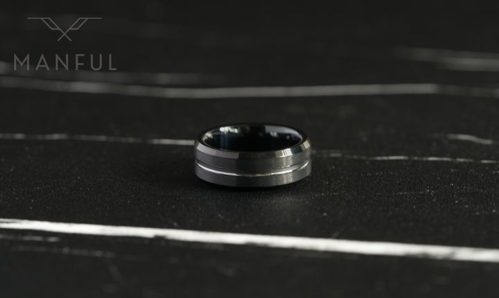 Black and Silver Tungsten Ring, lying flat on a dark marble surface in close-up