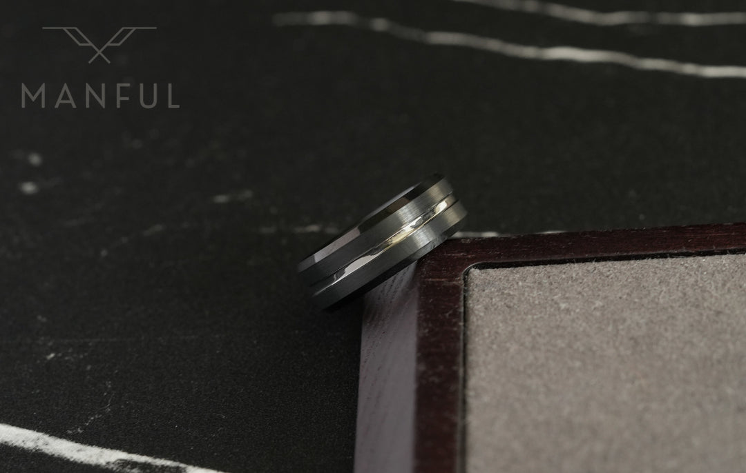 Black and Silver Tungsten Ring, propped against a wooden book edge on a dark marble surface