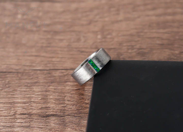 Black & Green Opal Line Tungsten Band, leaning against a dark wood block on a wood surface