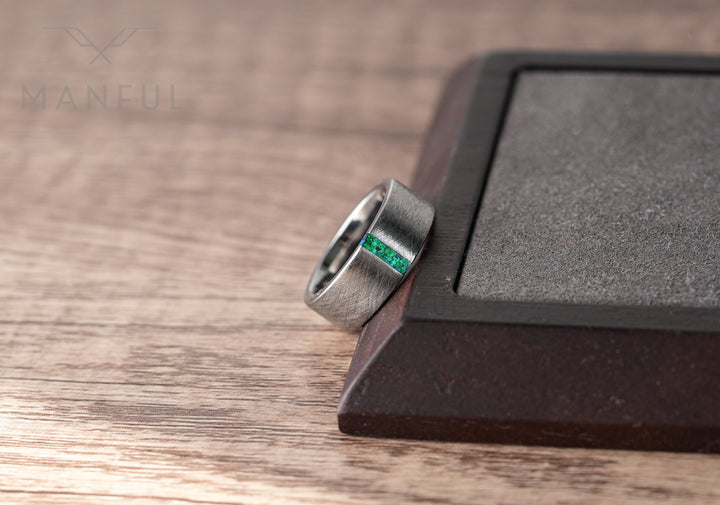 Black & Green Opal Line Tungsten Band, close-up leaning against a dark wood block on a wood surface