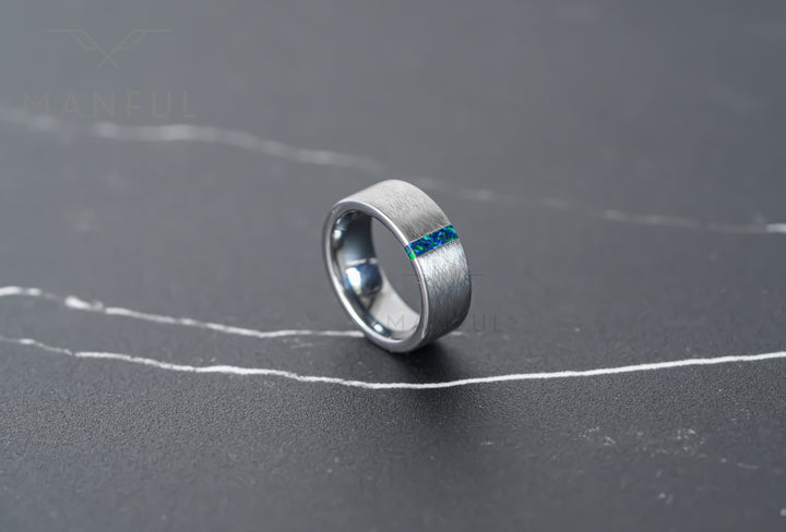 Black & Green Opal Line Tungsten Band, standing at an angle on grey marble showing the inlay