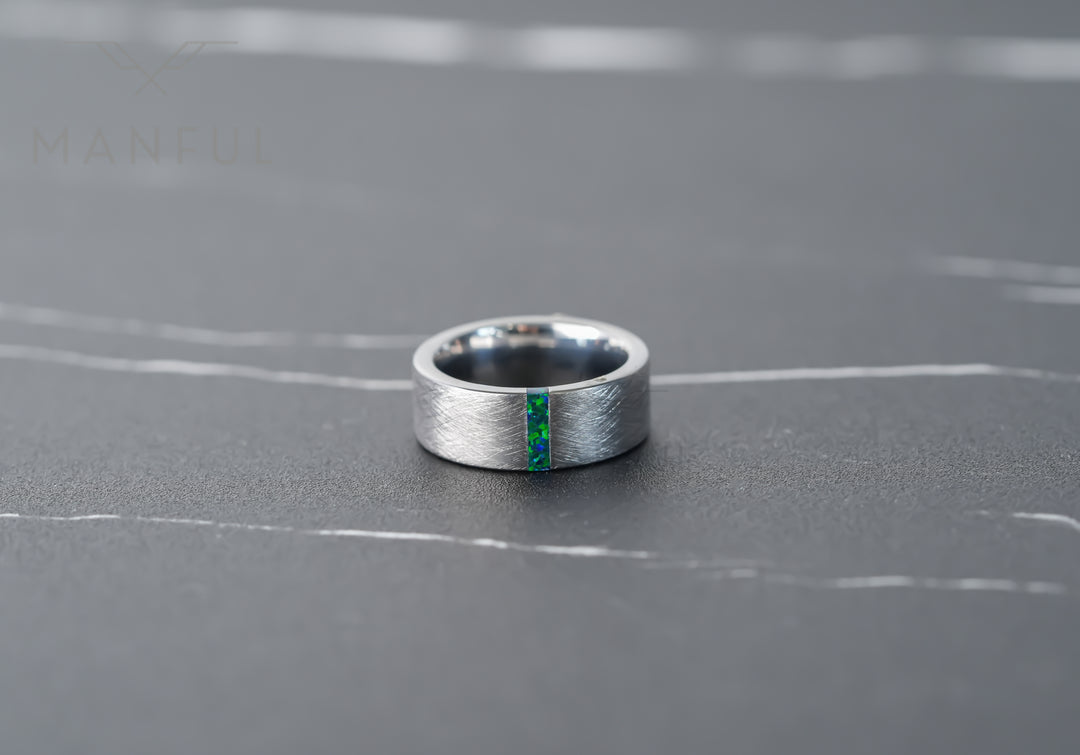 Black & Green Opal Line Tungsten Band, lying flat on grey marble in sunlight with the inlay facing forward