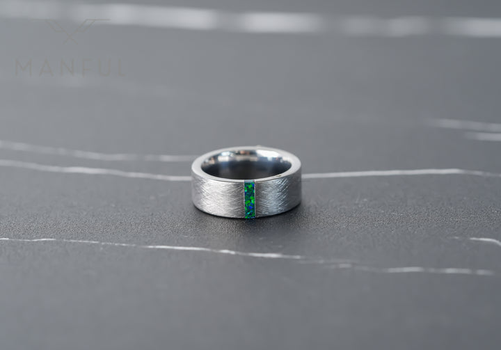 Black & Green Opal Line Tungsten Band, lying flat on grey marble in sunlight with the inlay facing forward