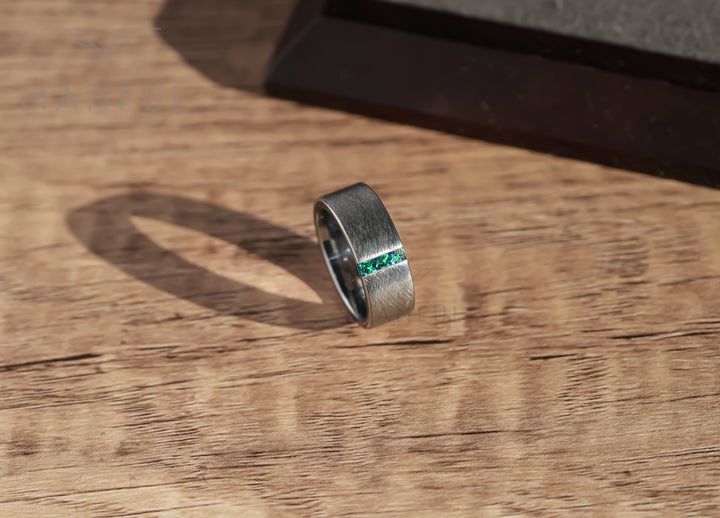 Black & Green Opal Line Tungsten Band, leaning against a dark wood block on a sunlit wood surface with a cast shadow