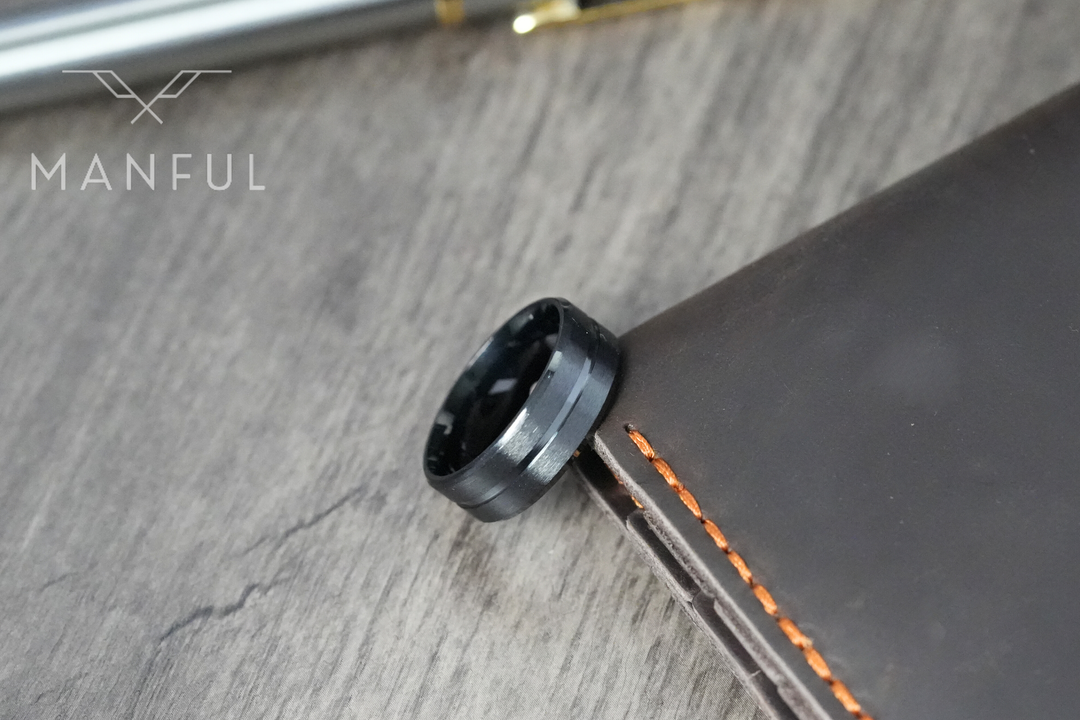 Black Onyx Band, resting on the edge of a brown leather notebook beside pens on a wood desk