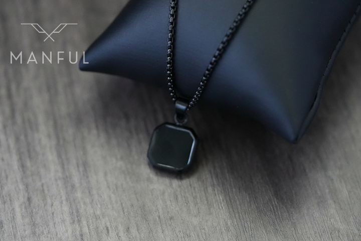 Onyx Square Necklace Black, close-up draped over a dark leather cushion prop