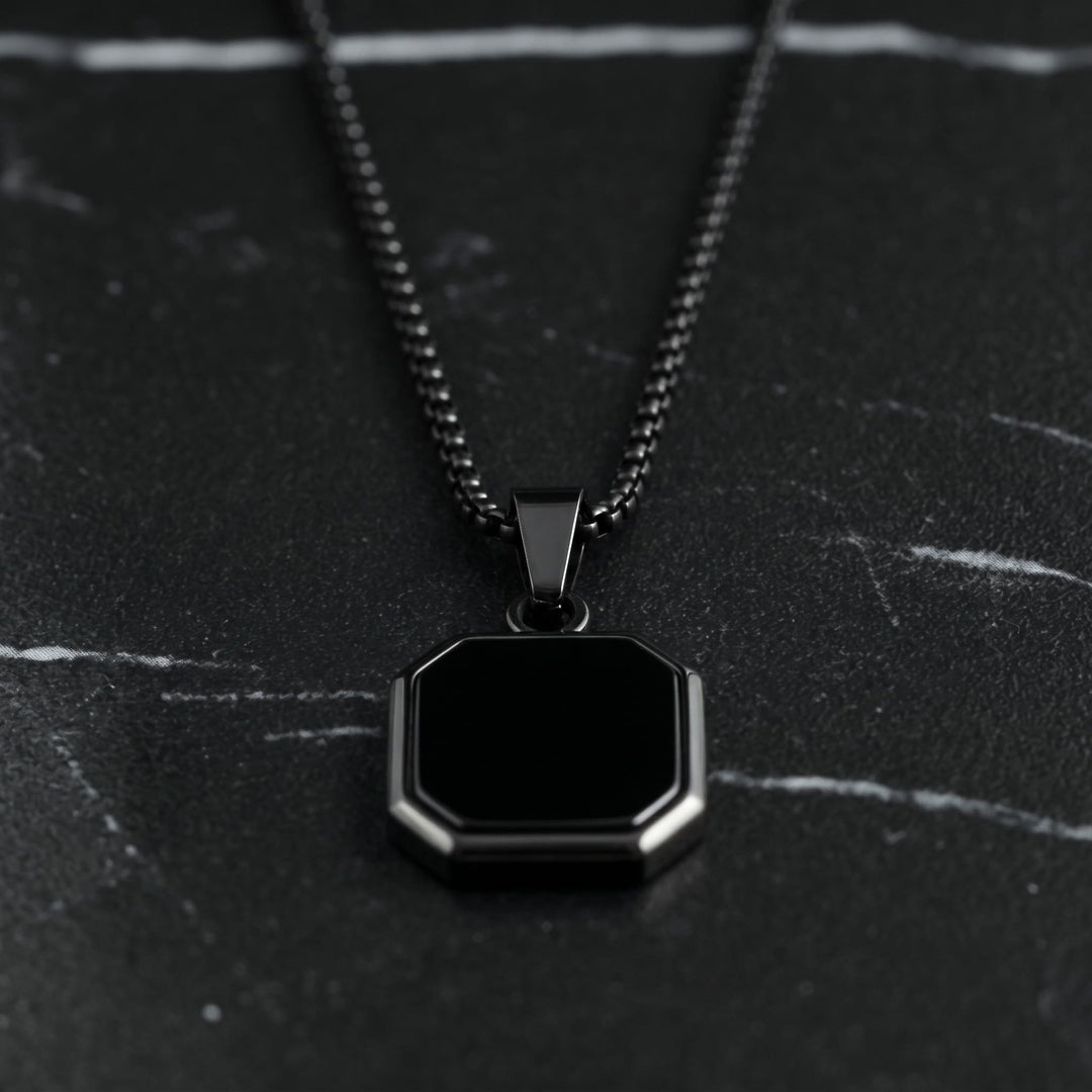 Onyx Square Necklace (Black) lying on dark marble with the black chain leading up