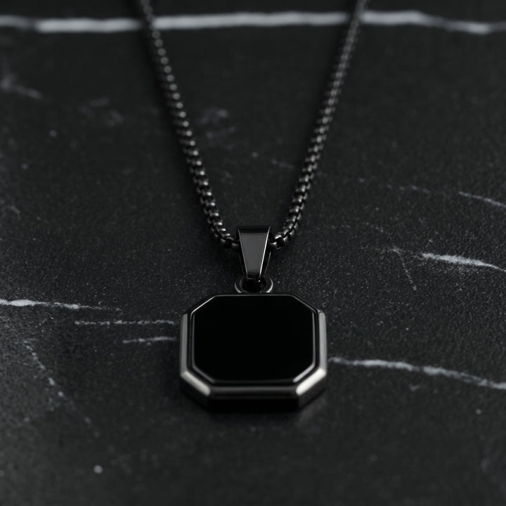 Onyx Square Necklace (Black) lying on dark marble with the black chain leading up