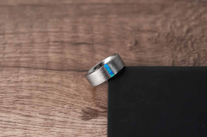 Azure Opal Line Tungsten Band, resting on a wooden surface propped against a black block