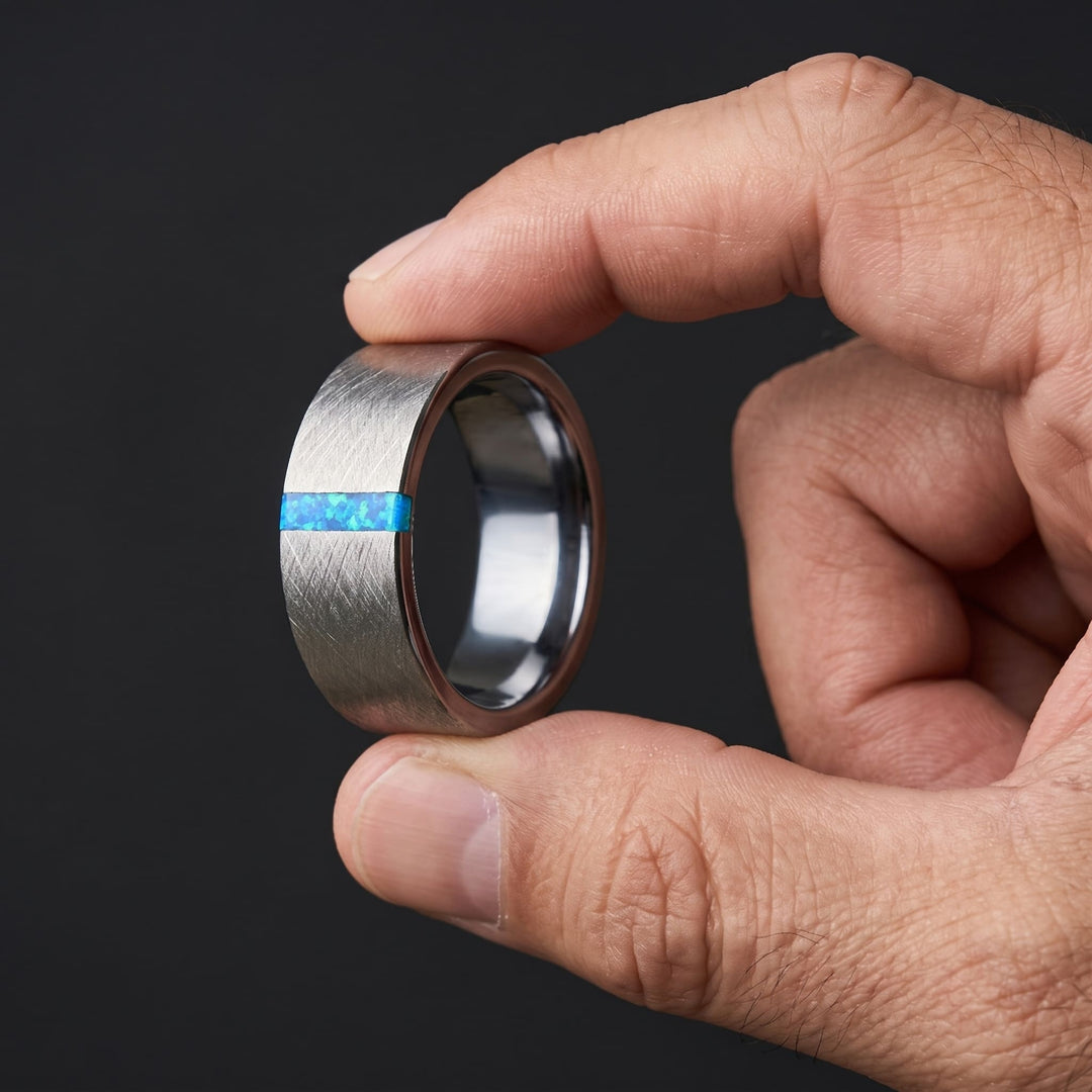 Azure Opal Line Tungsten Band held up between a man's thumb and finger