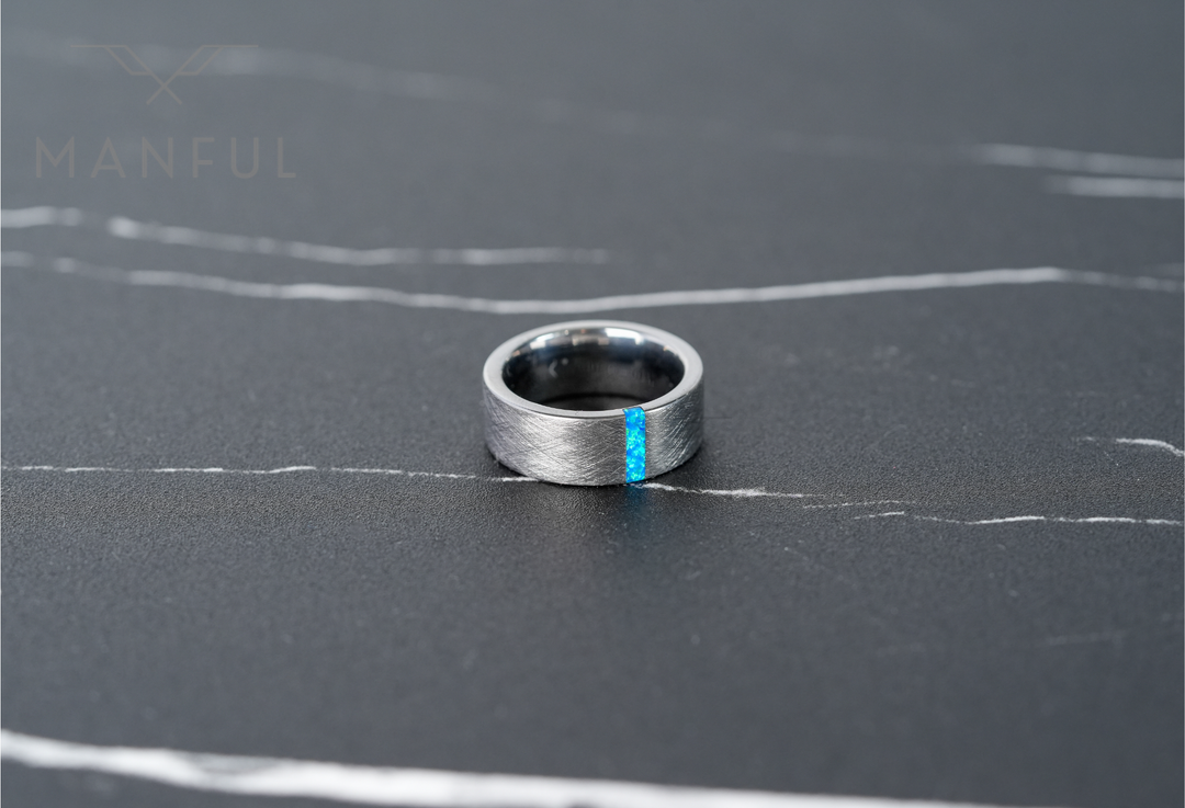 Azure Opal Line Tungsten Band, laid on a dark marble surface with white veining, close-up from above