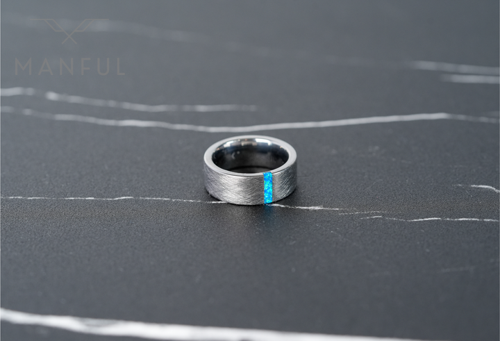 Azure Opal Line Tungsten Band, laid on a dark marble surface with white veining, close-up from above