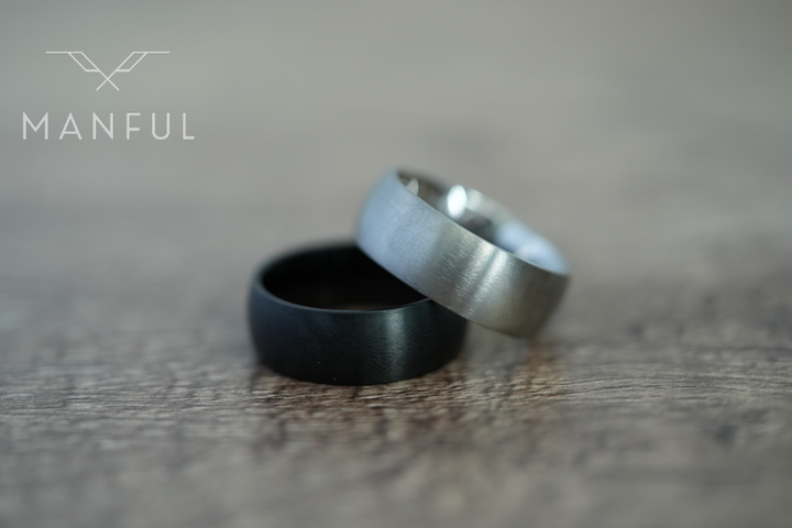 Brushed Titanium Band Black, lying beside a silver titanium band on a wood surface