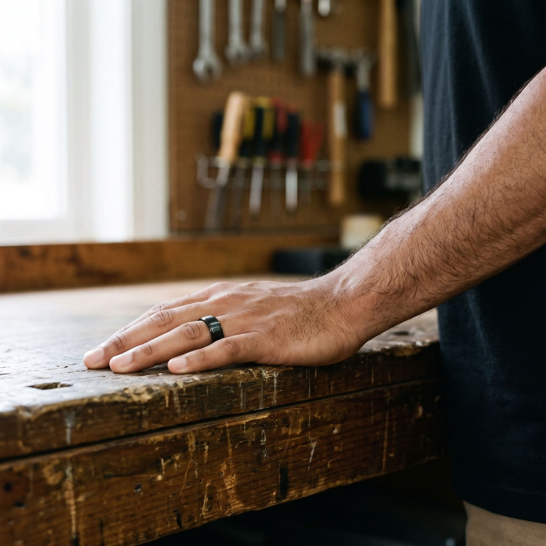 Brushed Tungsten Band (Black) on a man's finger, his hand resting on a workbench