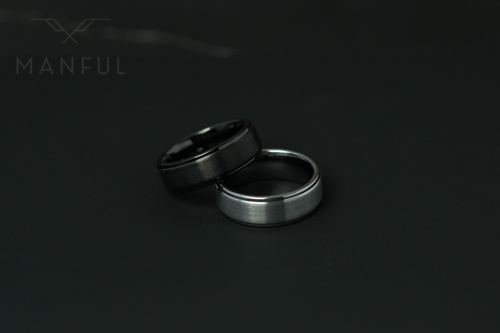 Brushed Tungsten Band Black, close-up beside the silver version resting together on a dark background