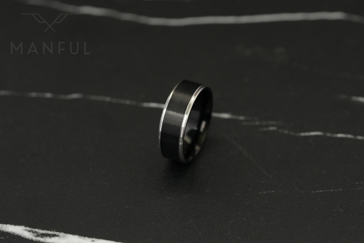 Brushed Tungsten Black & Silver Band, standing on a dark marble surface in soft focus