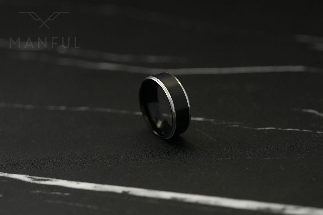 Brushed Tungsten Black & Silver Band, lying tilted on a dark marble surface in soft focus