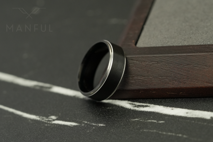 Brushed Tungsten Black & Silver Band, propped against the edge of a dark wooden block