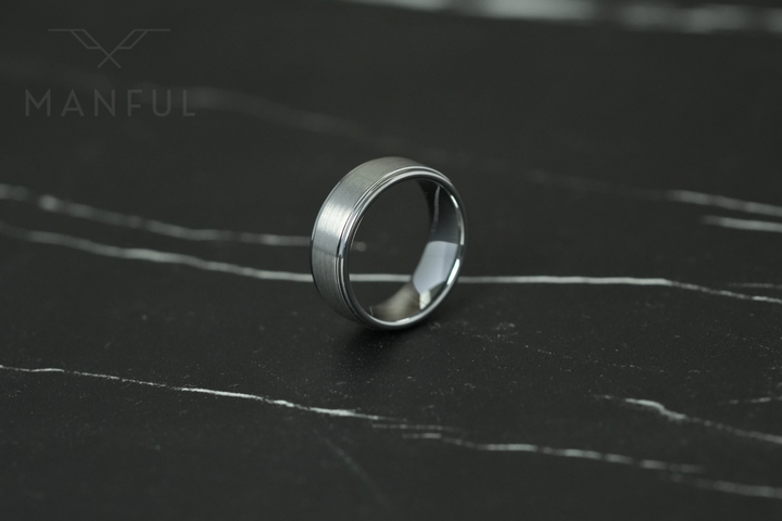 Brushed Tungsten Band Silver, lying on dark marble, leaning left