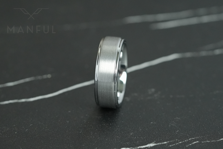 Brushed Tungsten Band Silver, lying on dark marble, leaning right in close-up