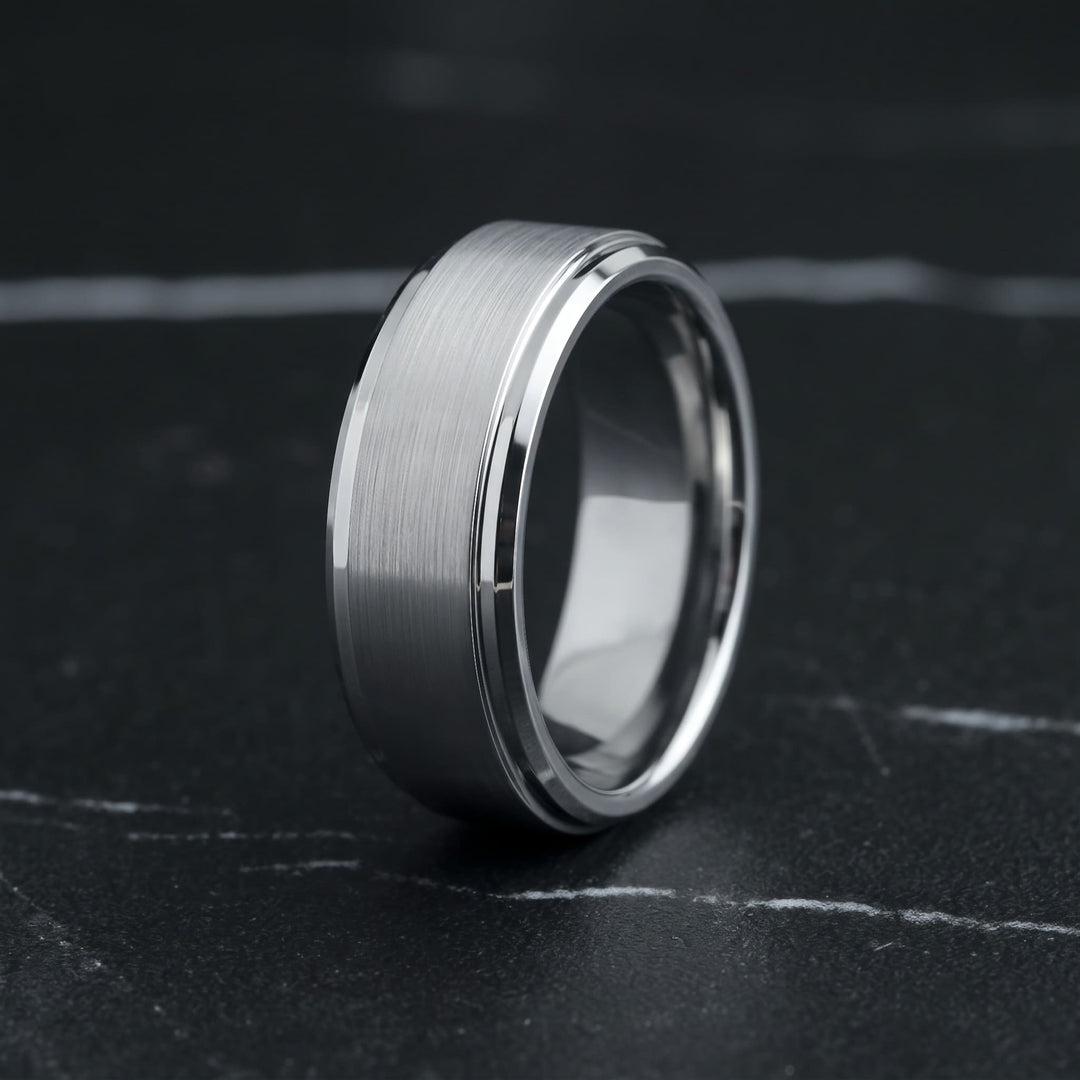Brushed Tungsten Band (Silver) standing upright on black marble with thin white veins