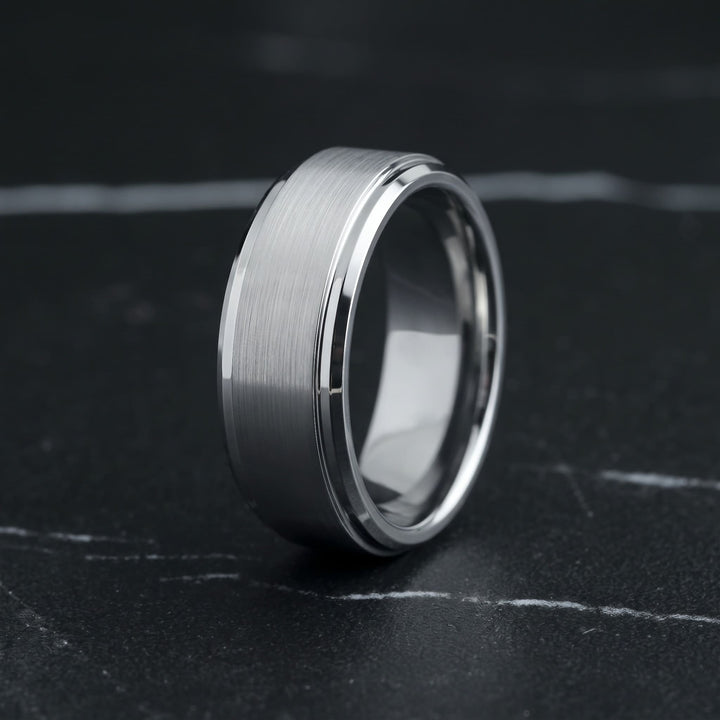 Brushed Tungsten Band (Silver) standing upright on black marble with thin white veins