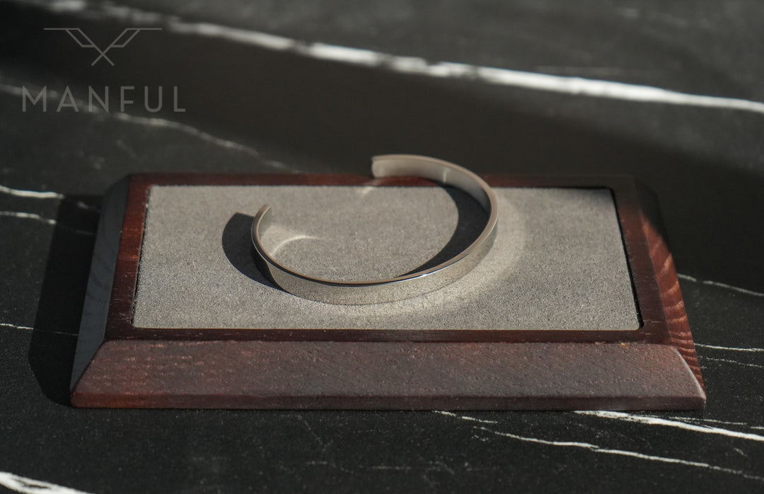 Adjustable Bangle Silver, sitting open on a rectangular stone and wood stand on dark marble