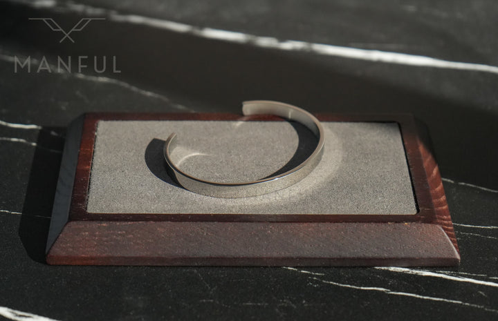 Adjustable Bangle Silver, sitting open on a rectangular stone and wood stand on dark marble