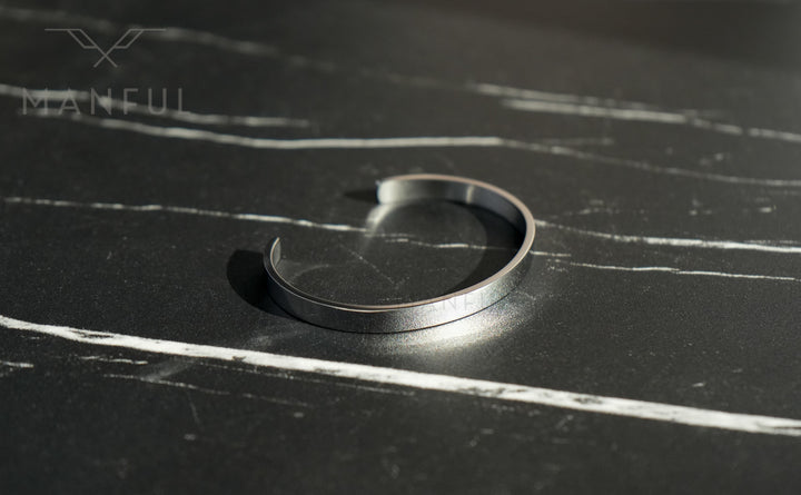 Adjustable Bangle Silver, lying open directly on a dark marble surface with pale veining