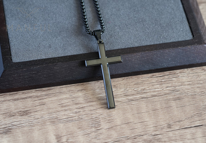 Cross Pendant Necklace Black, resting at an angle on a wooden tray with a grey suede insert